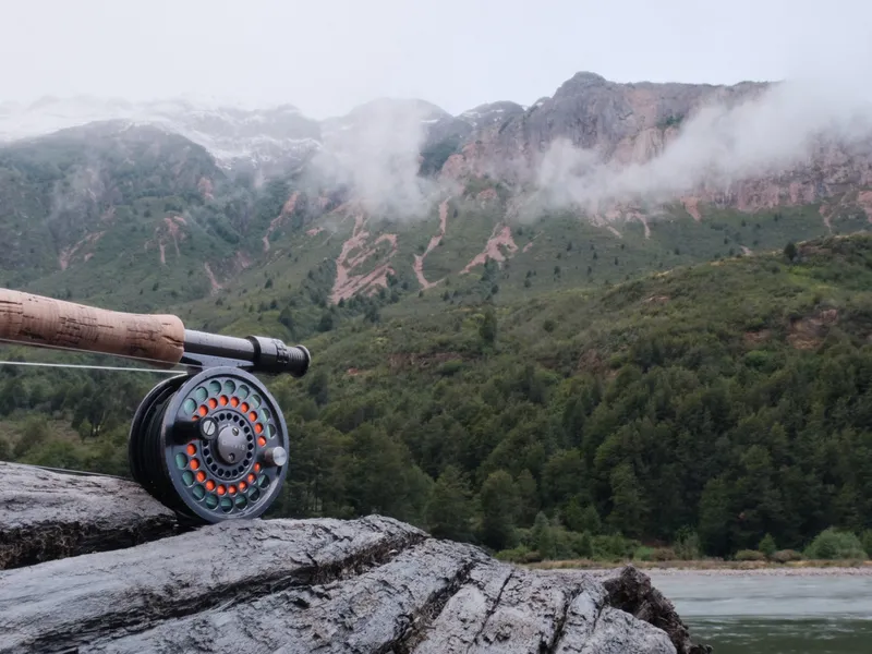 Fly reel on river rock, Patagonia mountains in mist