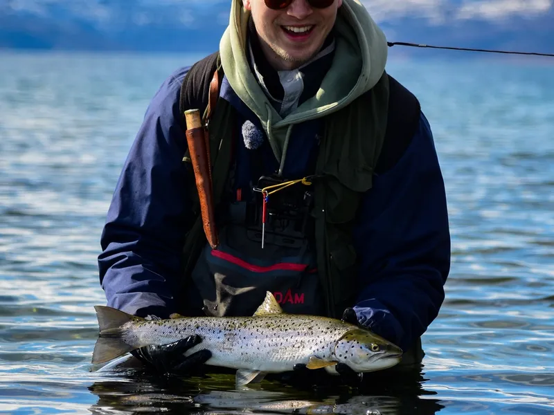 An angler with a sea trout, snowy peaks across the fjord