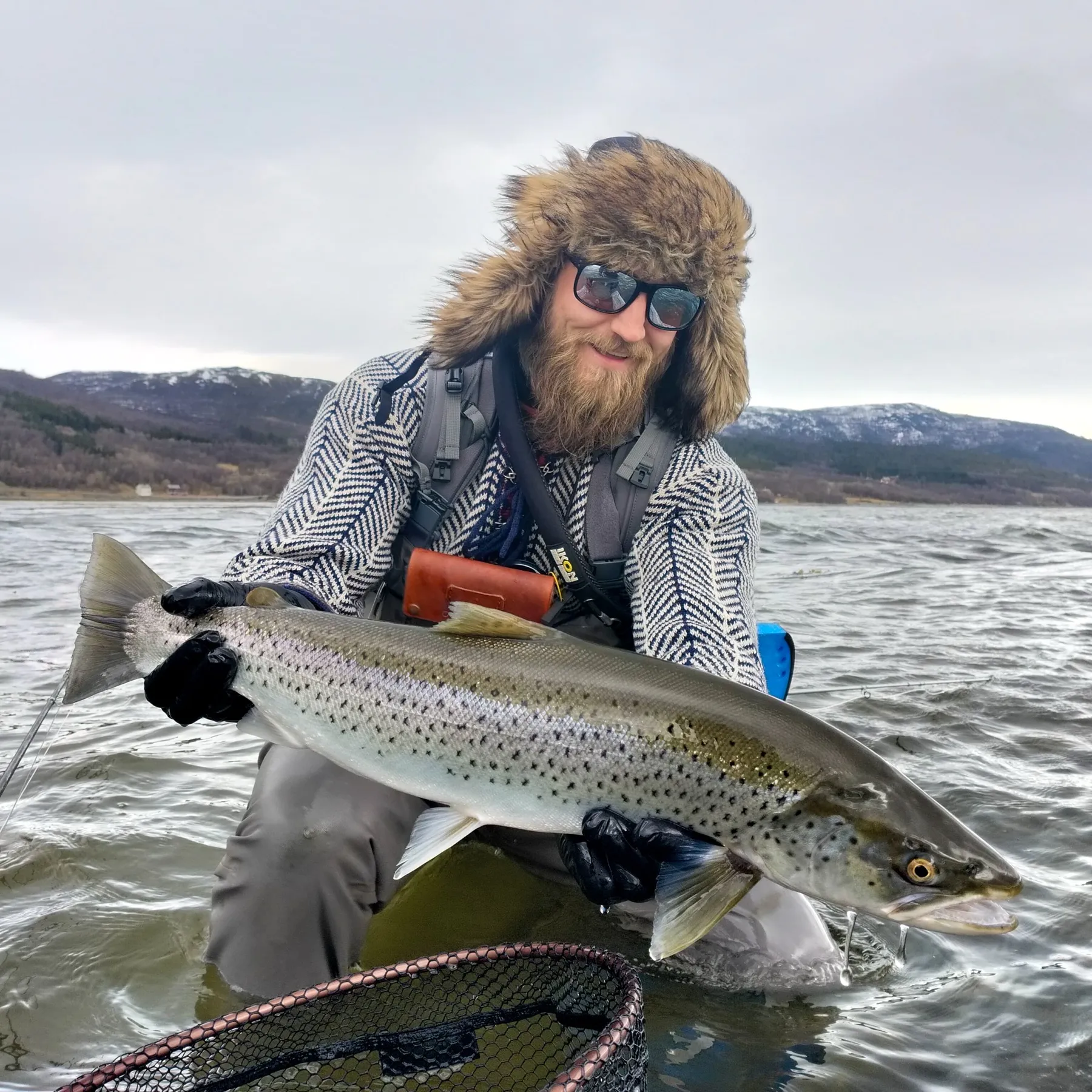 An angler kneeling in the fjord with a big silver sea trout
