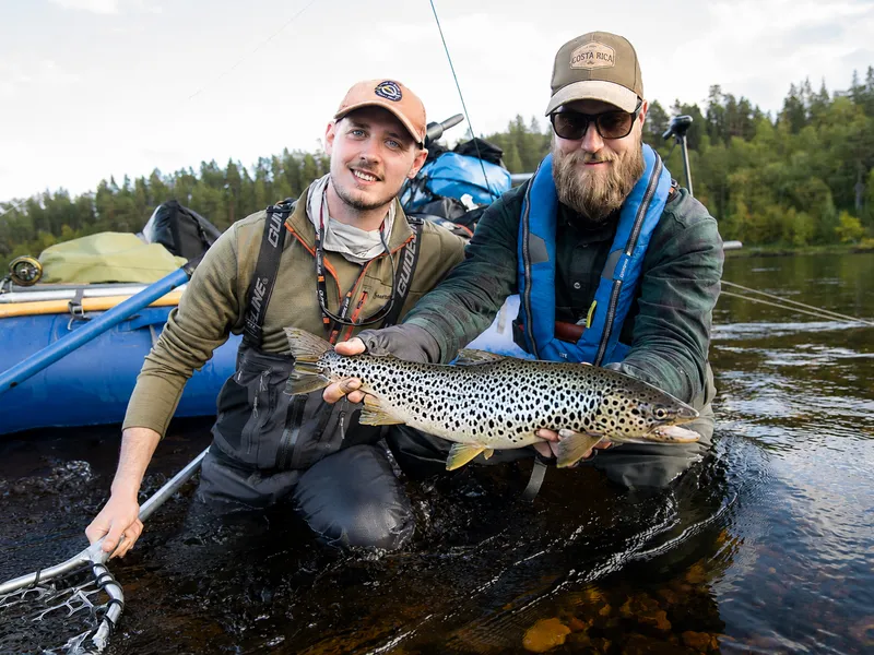 Two anglers and a brown trout beside the raft