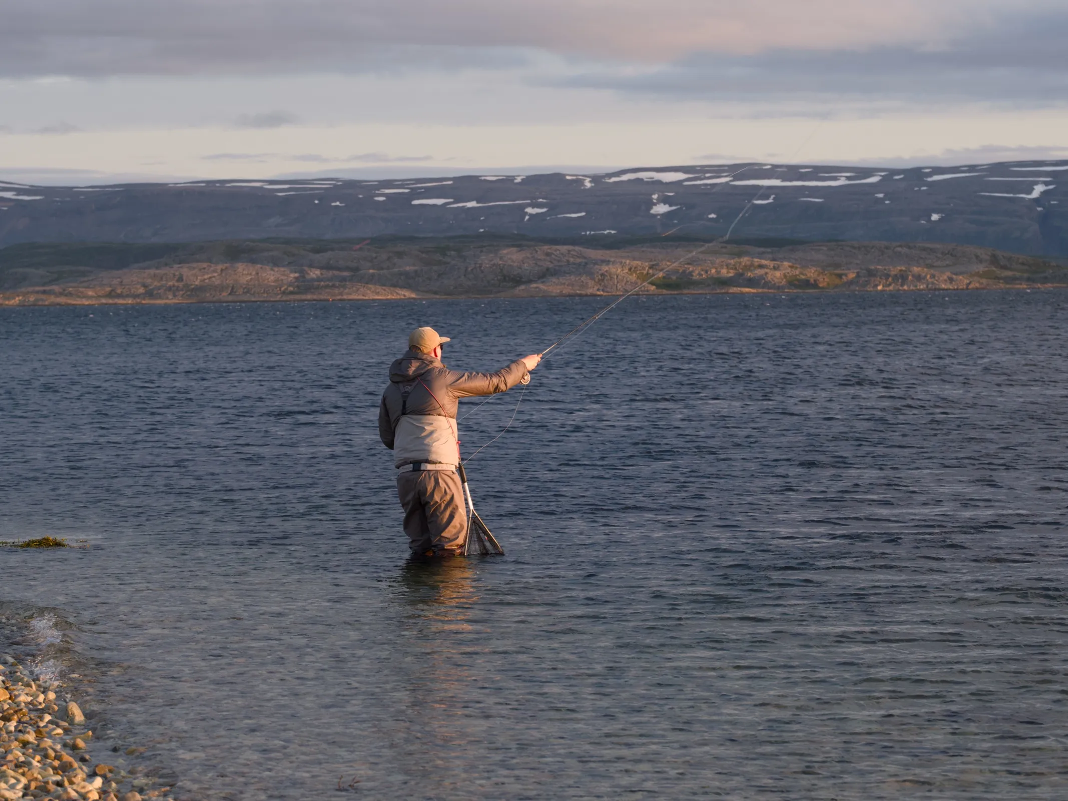 Casting from the shallows in low evening sun, snow patches on the hills across the water