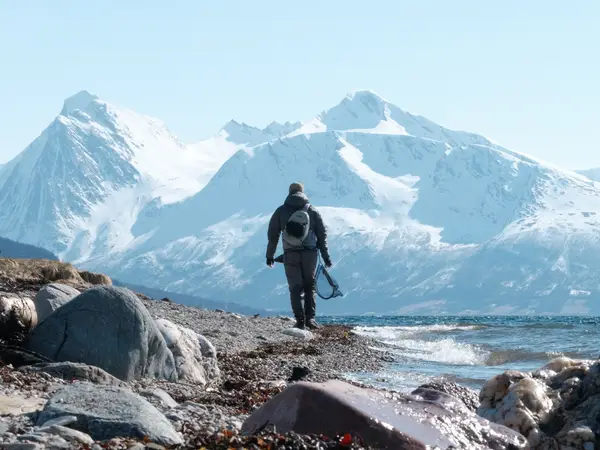 Walking an Arctic beach with a net, snow-covered peaks across the fjord